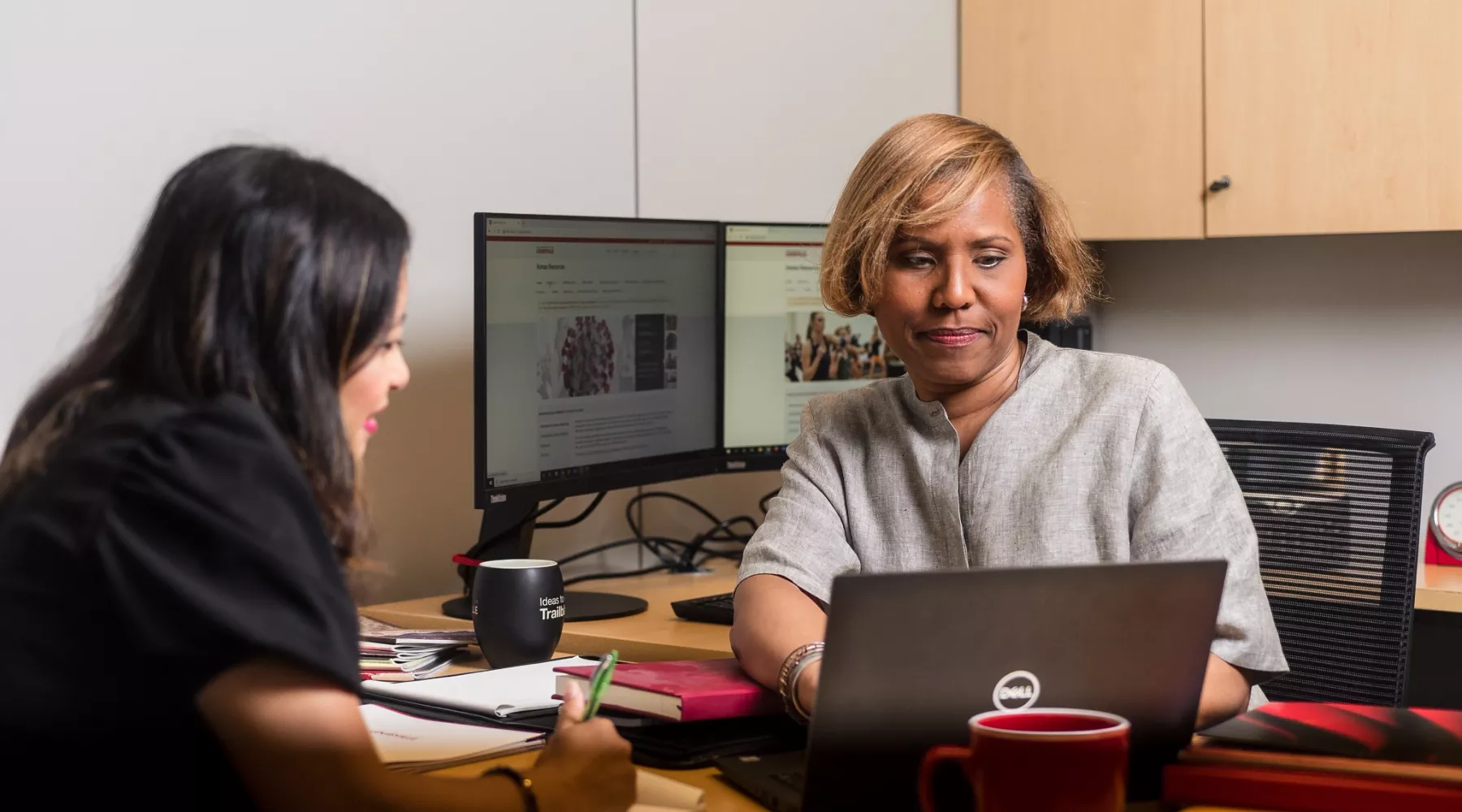 Two female employees seated during a meeting discussing content on screen of laptop