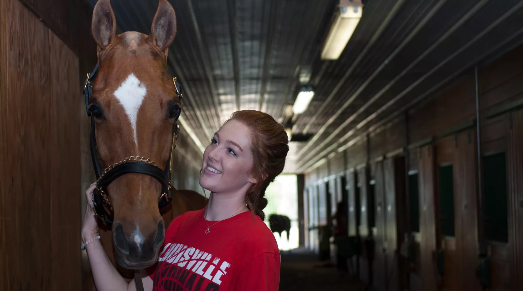 UofL College of Business student stands next to a light brown horse