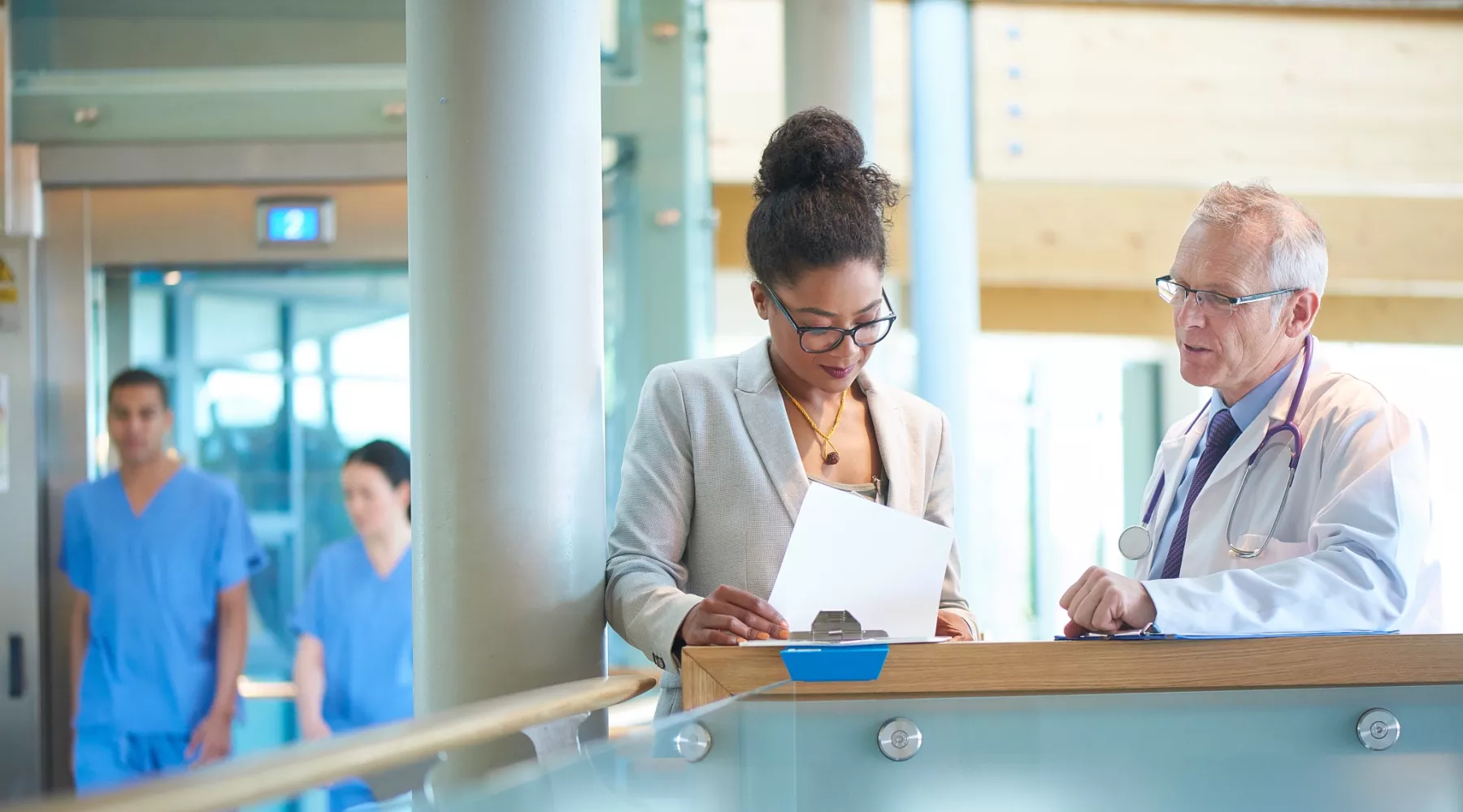 A woman and a doctor  on a stairwell of a modern hospital discussing case notes