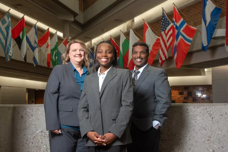 Sakthiraj Kandasamy, Susan Miracle and Hope Odubena in front of flags in College of Business atrium.