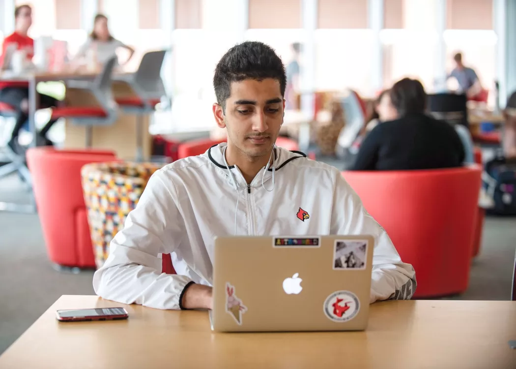Student working on laptop in common area on UofL campus