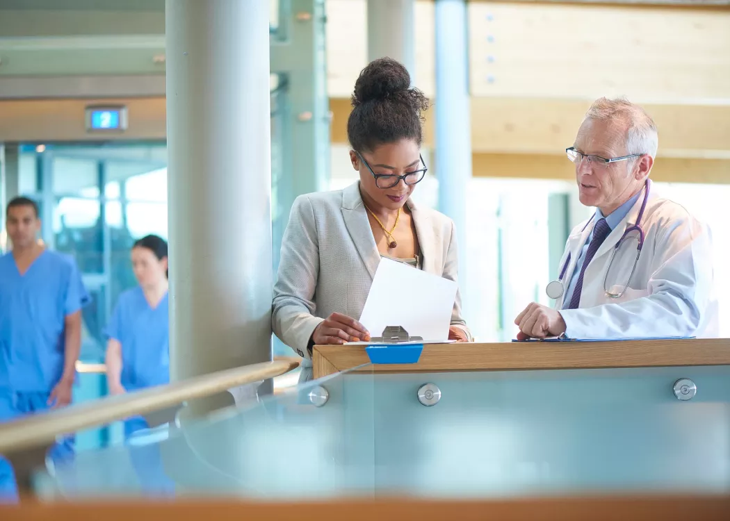 A woman and a doctor  on a stairwell of a modern hospital discussing case notes