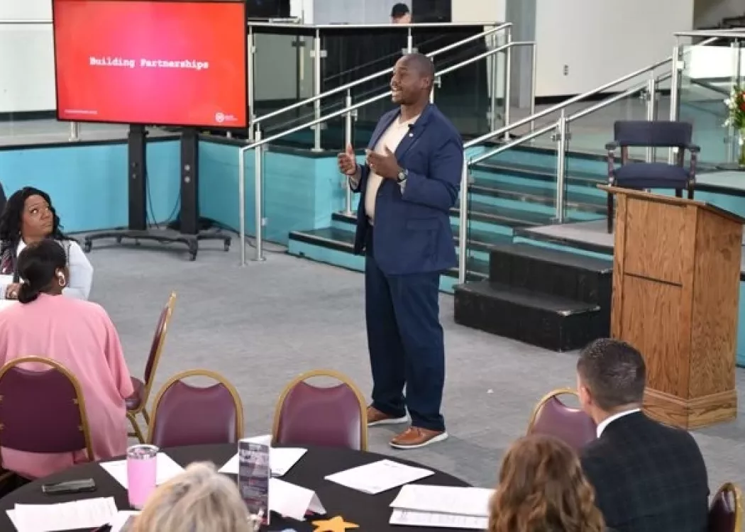 A suited man delivering a presentation in front of a crowd.