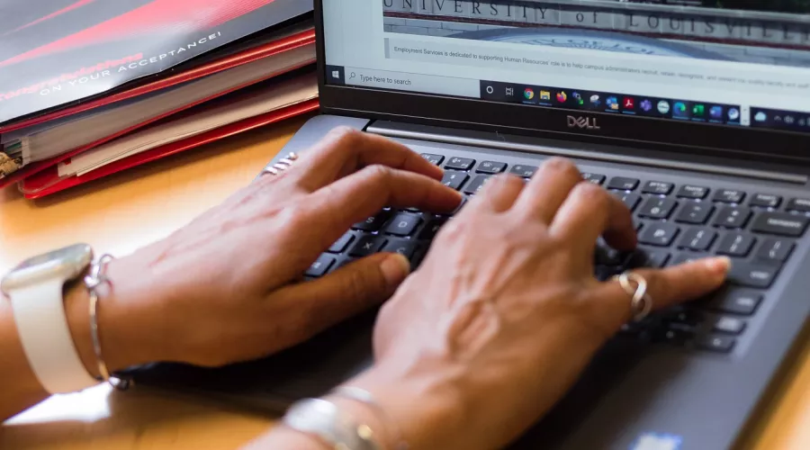 Employee typing on laptop in a UofL office