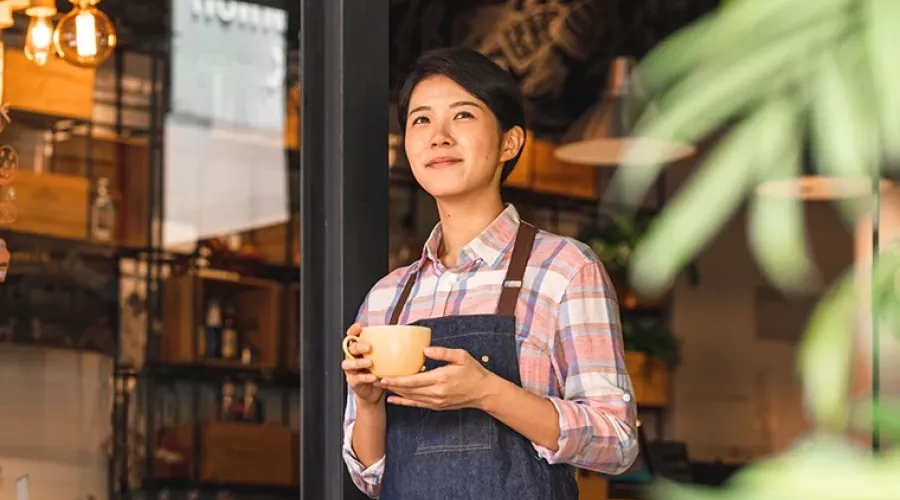 Woman holds a cup of coffee while looking out from the front of a store