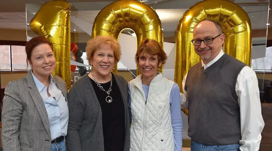 Four people standing in front of balloons.