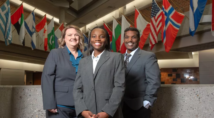Sakthiraj Kandasamy, Susan Miracle and Hope Odubena in front of flags in College of Business atrium.