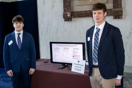 Two men standing in front of a computer monitor displaying a presentation.