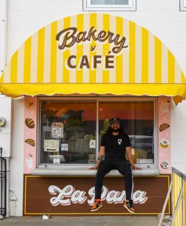 Co-owner Joshua Gonzalez sits atop the counter outside La Pana Bakery y Café